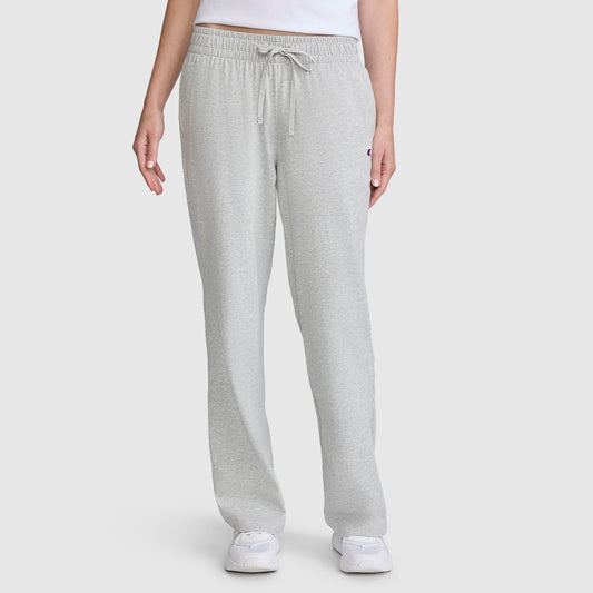 A person wearing Champion Lightweight Lounge Pants, C Logo in light gray, along with a white shirt and white sneakers, stands against a plain white background. Only the lower torso and legs are visible.