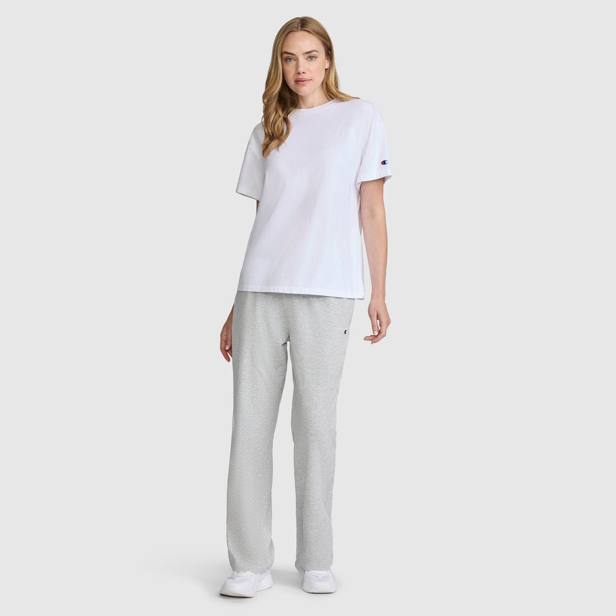 A woman wearing a plain white short-sleeved t-shirt, Champion Lightweight Lounge Pants, C Logo in grey, and white sneakers.