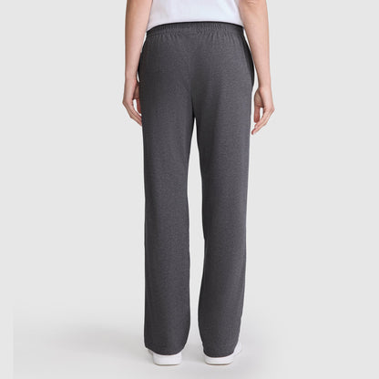 A person stands with their back to the camera, wearing Champion’s Lightweight Lounge Pants, C Logo—dark gray, straight-leg, ultra-soft lounge pants featuring an elastic waistband for comfort—with a white top. The background is plain and light-colored.