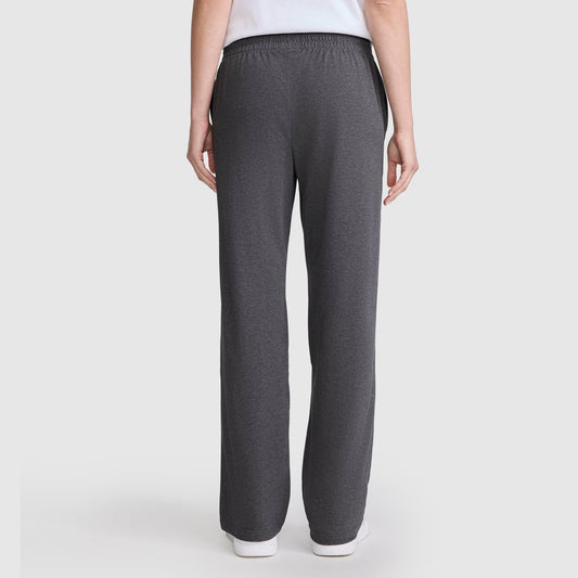A person stands with their back to the camera, wearing Champion’s Lightweight Lounge Pants, C Logo—dark gray, straight-leg, ultra-soft lounge pants featuring an elastic waistband for comfort—with a white top. The background is plain and light-colored.