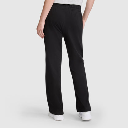 A person stands with their back to the camera, wearing Champion Lightweight Lounge Pants, C Logo in black. The lounge pants are crafted from soft jersey cotton and feature an elastic waistband for a relaxed fit. They are styled with white sneakers and a light-colored top. The background is plain and light-colored.