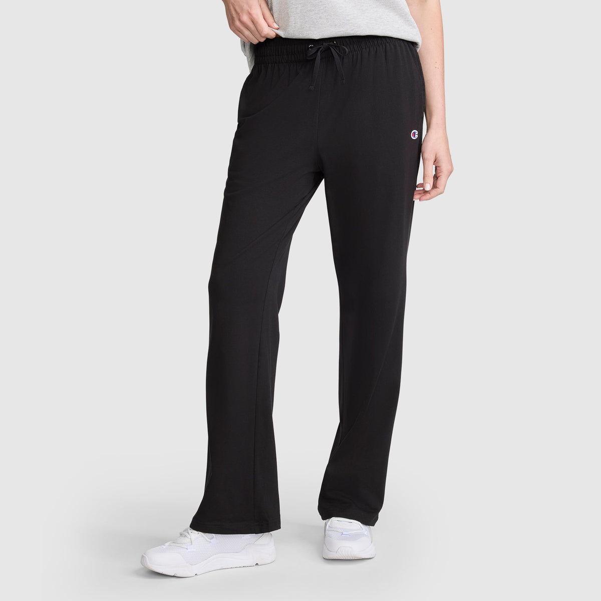 A person wears Champion Lightweight Lounge Pants, featuring a drawstring waist and the brand’s signature C logo on the left thigh; they pair them with white sneakers.