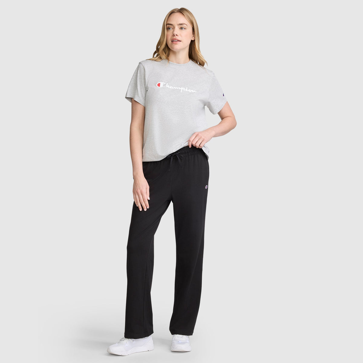 A woman wearing a gray t-shirt and Champion Lightweight Lounge Pants, C Logo, which are lightweight jersey cotton lounge pants with a drawstring waist.