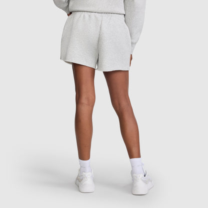 A person shown from the back wears light gray Champion 3" Powerblend Shorts, C Logo for women, a matching sweatshirt, white socks, and white sneakers. The background is plain white.