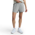 A person stands against a white background wearing a light grey T-shirt, Champion Practice Shorts, white socks, and white sneakers. The image is cropped at the shoulders so the face is not visible.