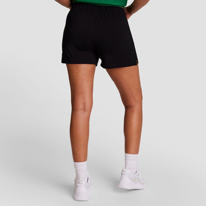 Person standing with back to camera wears a green top and Champion Practice Short—ideal women’s shorts—paired with white socks and sneakers, set against a plain light background.