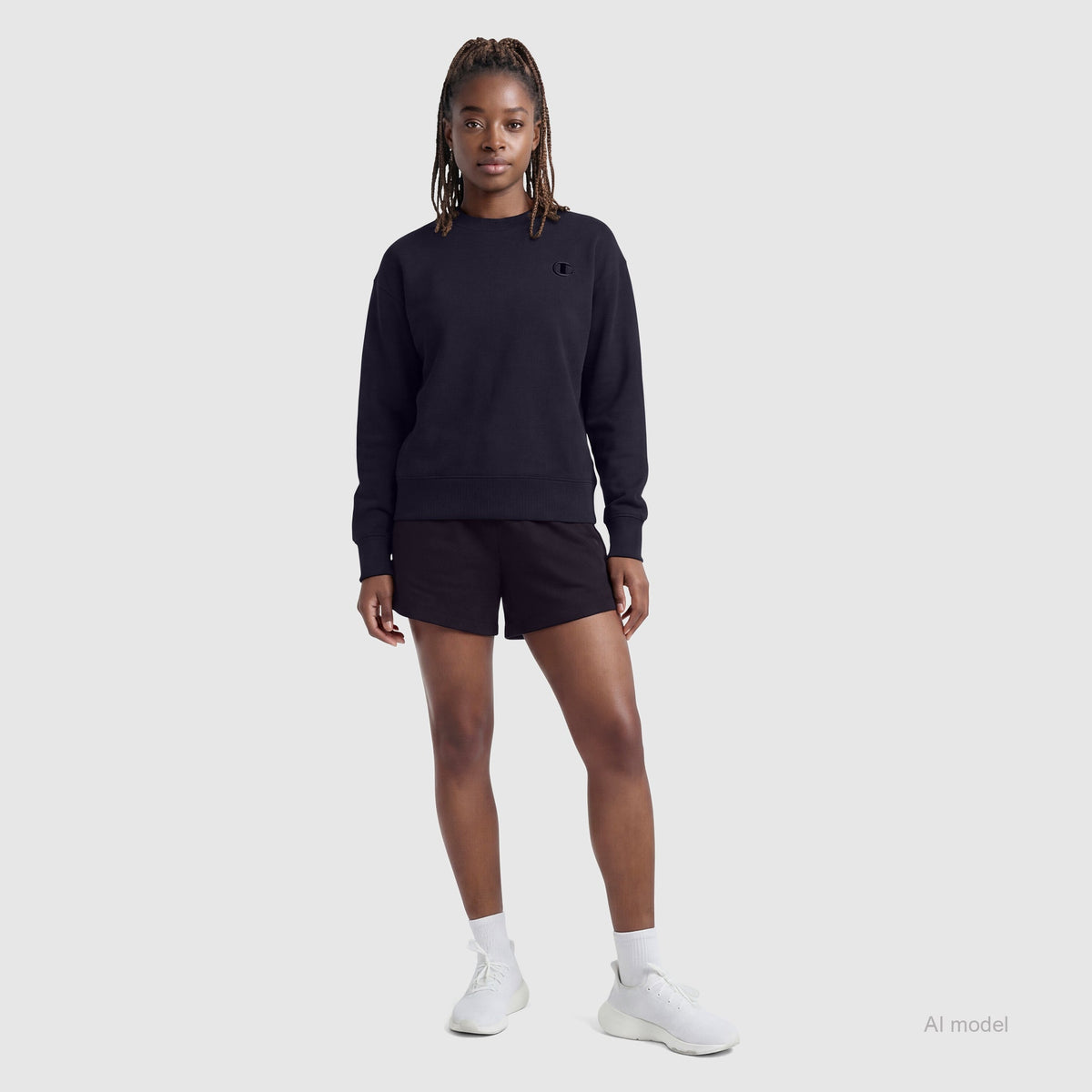 A person with long, braided hair wears a black sweatshirt and the Champion 4" Lightweight Lounge Shorts with C Logo—featuring an adjustable waistband—paired with white socks and white sneakers, standing against a plain light gray background.