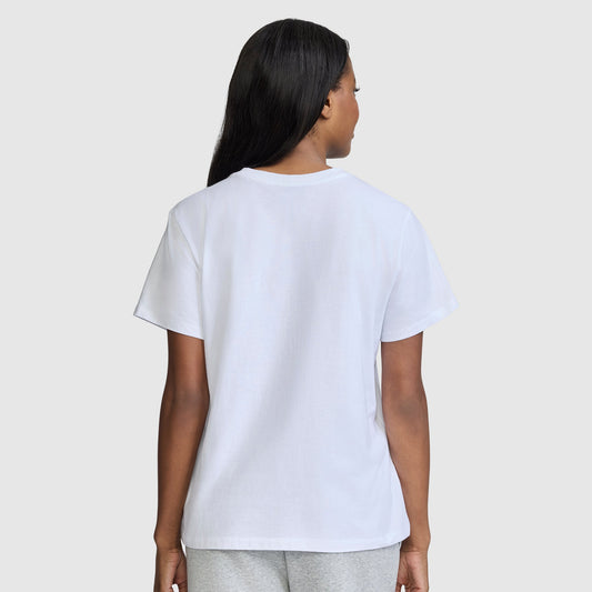 A person with long dark hair is standing and facing away, wearing a plain white Champion Classic T-Shirt, Script Logo paired with light gray pants, against a light gray background.