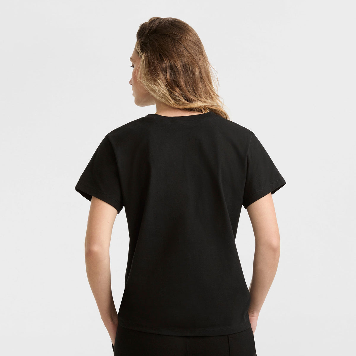 Person with light brown hair wearing a Champion Classic T-Shirt, Script Logo in plain black, facing away from the camera against a plain white background.