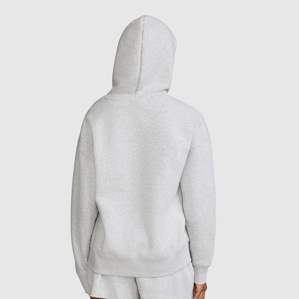 A person is seen from behind wearing a light gray Champion Tonal Script Freshman Powerblend Hoodie with matching shorts, displaying the back of the women’s hooded sweatshirt against a plain light background.