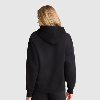 A person with light brown hair is shown from the back, wearing a Champion Tonal Script Freshman Powerblend Hoodie and black pants. The midweight fleece sweatshirt stands out against the light gray background.