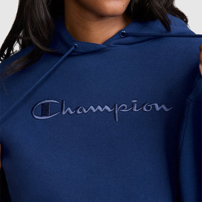 A person is wearing a blue Champion Tonal Script Freshman Powerblend Hoodie, crafted from soft midweight fleece, featuring the Champion logo embroidered in tonal script across the chest.