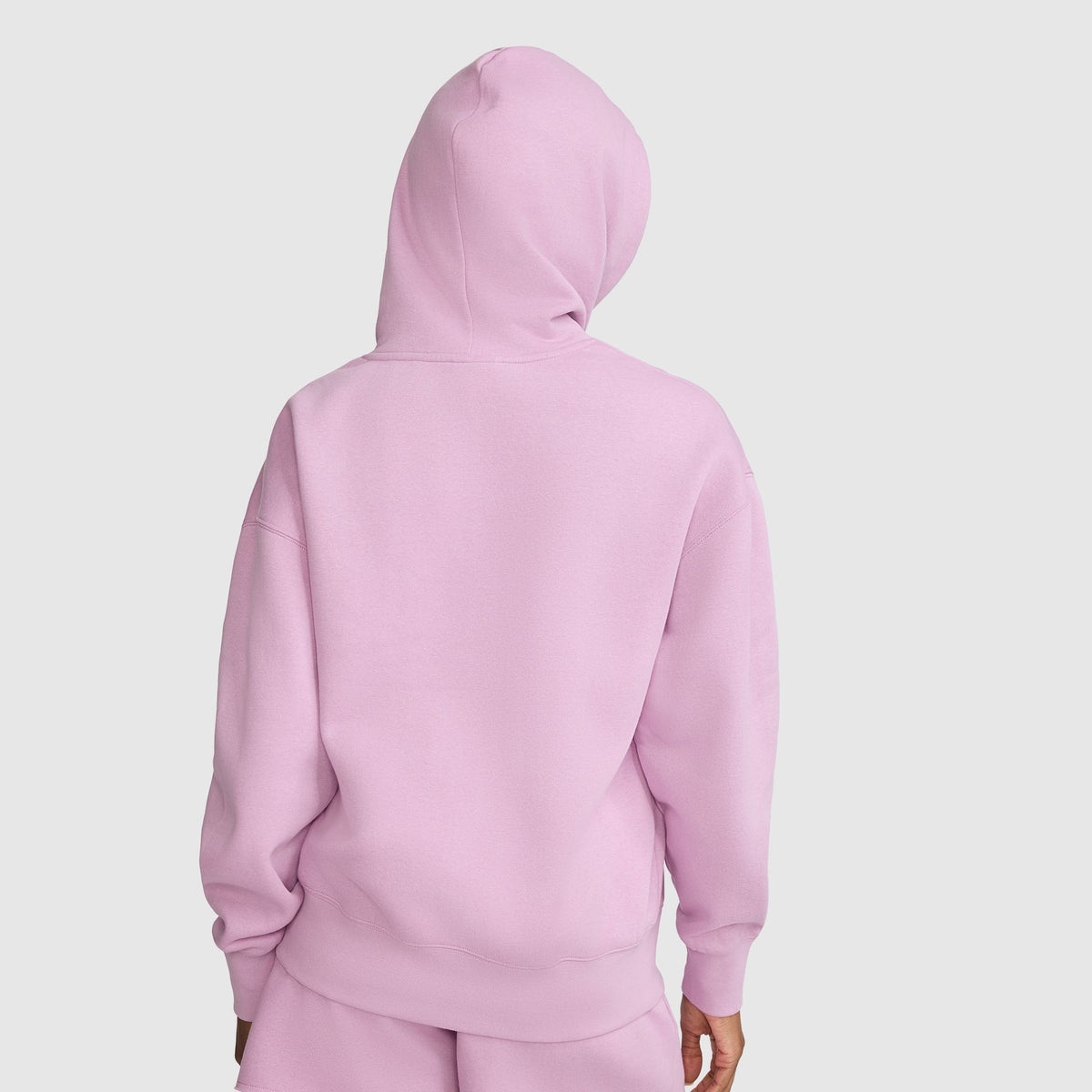 A person is shown from the back, standing against a plain white background, wearing the Champion Tonal Script Freshman Powerblend Hoodie in light pink with matching pants.