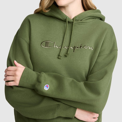 A person wears the Champion Tonal Script Freshman Powerblend Hoodie in olive green, featuring a logo on the chest. With arms folded and only the lower part of their face and torso visible, this cozy fleece sweatshirt blends comfort and style for a versatile casual look.