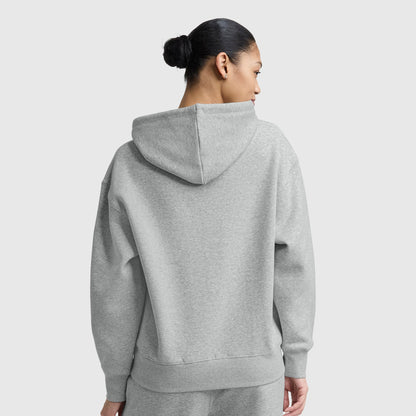A woman with dark hair in a bun, seen from behind, wears the Champion Small C Freshman Powerblend Hoodie and matching sweatpants in light gray midweight fleece against a plain light gray background.