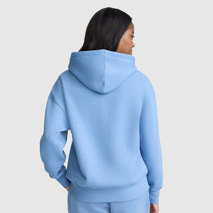 A person with long dark hair is wearing a light blue Champion Small C Freshman Powerblend Hoodie and matching pants, facing away from the camera against a plain light gray background.