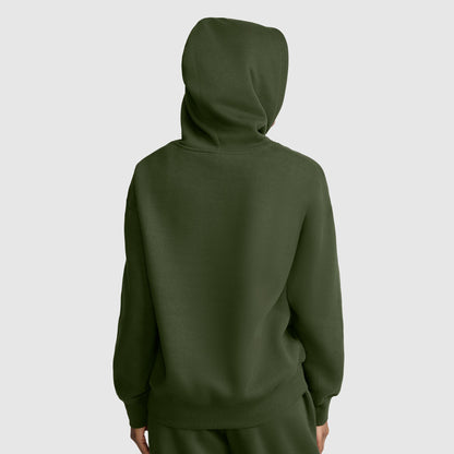 A person stands facing away with the hood up, wearing a dark green Champion Small C Freshman Powerblend Hoodie and matching pants, set against a plain light gray background.