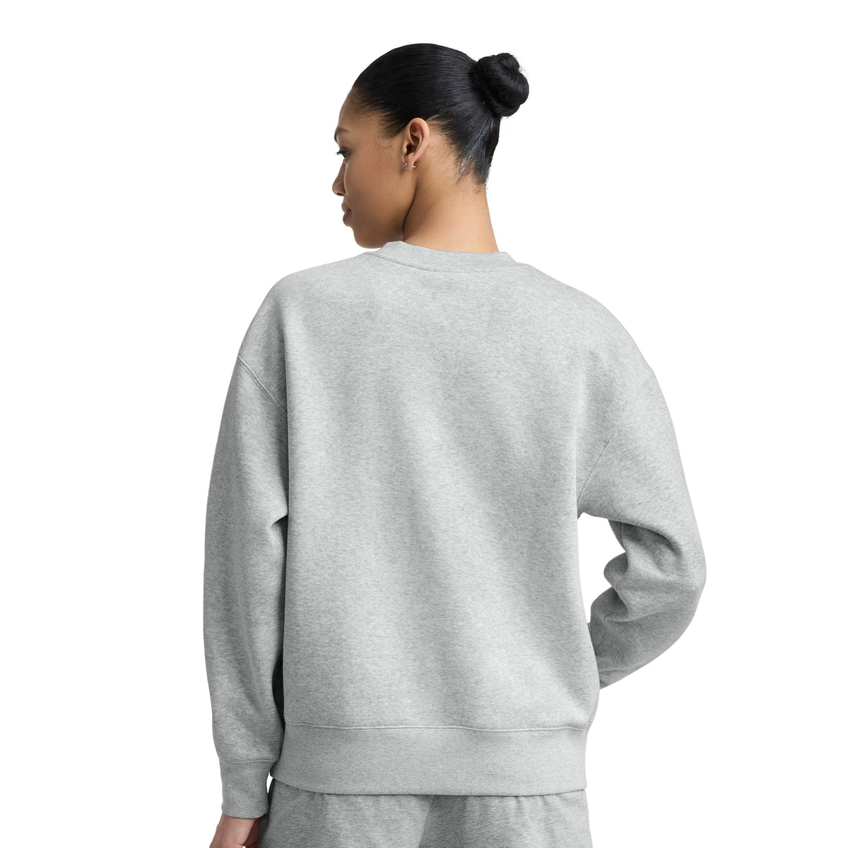 A person with dark hair in a bun is shown from behind wearing the Champion Powerblend Crewneck, Small "C," paired with light gray sweatpants, standing against a plain white background for a classic, comfortable look.