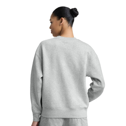 A person with dark hair in a bun is shown from behind wearing the Champion Powerblend Crewneck, Small "C," paired with light gray sweatpants, standing against a plain white background for a classic, comfortable look.