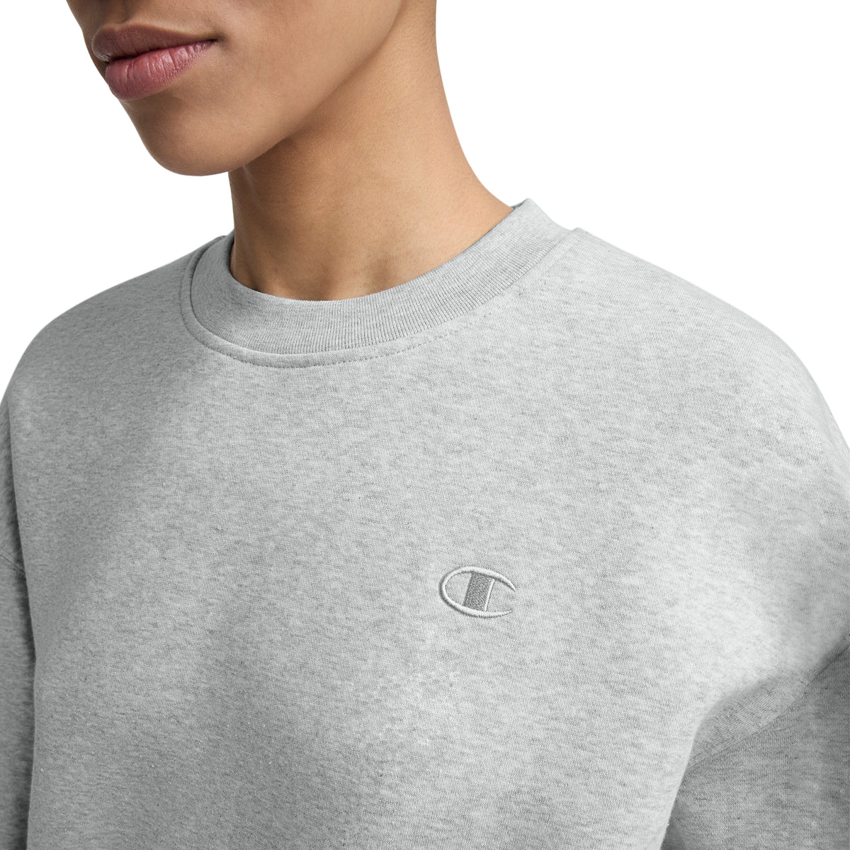 A person wearing a light gray Champion Powerblend Crewneck with a small embroidered "C" logo on the left chest; only their lower face, neck, and upper torso are visible.