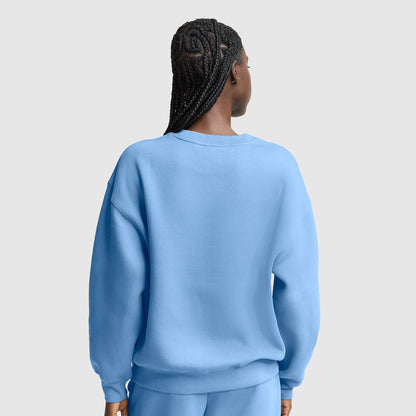 A person with braided hair, seen from behind, is wearing a loose, light blue Champion Powerblend Crewneck, Small “C” sweatshirt with matching pants against a plain light gray background.