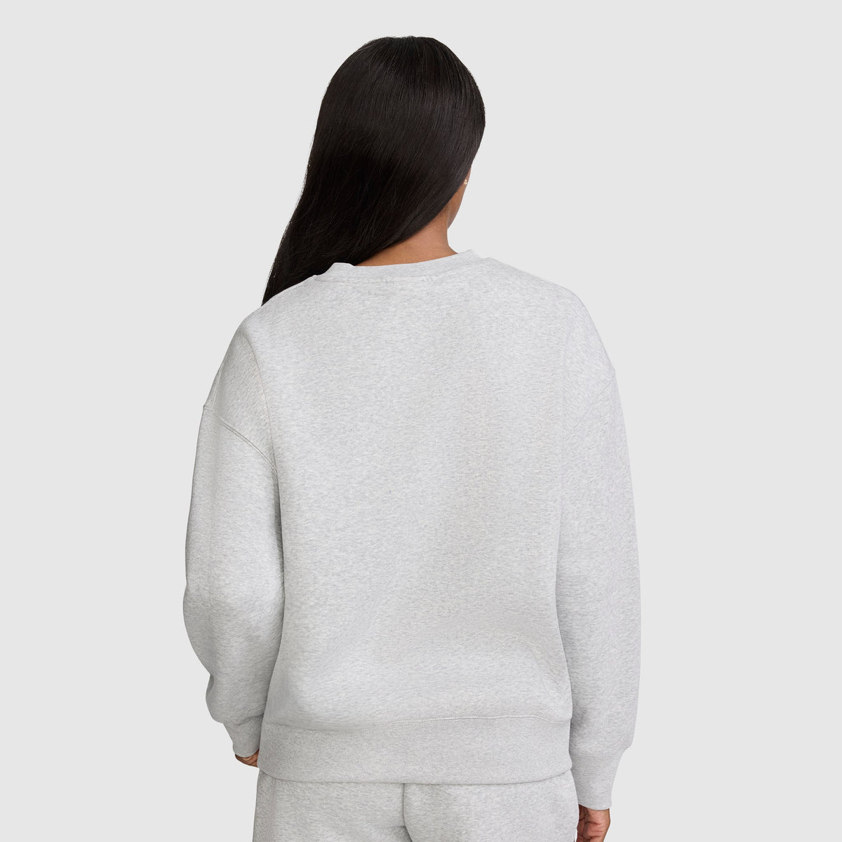 A person with long, straight dark hair is seen from the back, wearing a light gray Champion Powerblend Crewneck Sweatshirt with an embroidered script logo and matching sweatpants against a plain, light gray background, showcasing classic women's fashion in cozy fleece.