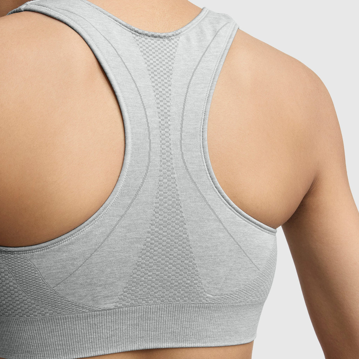 Close-up of a person’s upper back wearing the Champion Infinity Racerback Sports Bra in light gray, featuring seamless fabric with subtle patterns for support. This moderate support bra stands out against a plain white background.
