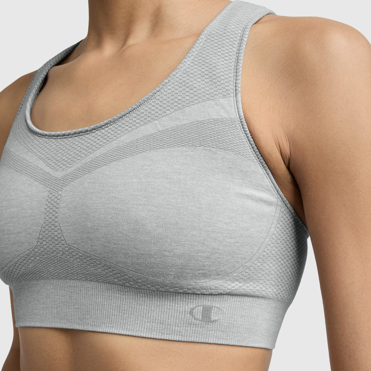 A close-up shows a person wearing the Champion Infinity Racerback Sports Bra in light gray with a textured, seamless design, highlighting the upper torso and shoulders against a plain background.
