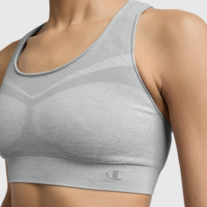 A close-up shows a person wearing the Champion Infinity Racerback Sports Bra in light gray with a textured, seamless design, highlighting the upper torso and shoulders against a plain background.