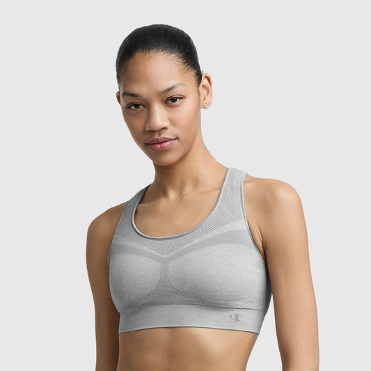 A woman with dark hair pulled back wears a light gray Champion Infinity Racerback Sports Bra and small stud earrings, standing against a plain white background.