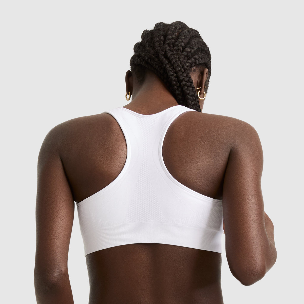 A woman with braided hair and gold hoop earrings models the Champion Seamless Racerback Sports Bra, shown from behind against a plain light gray background.