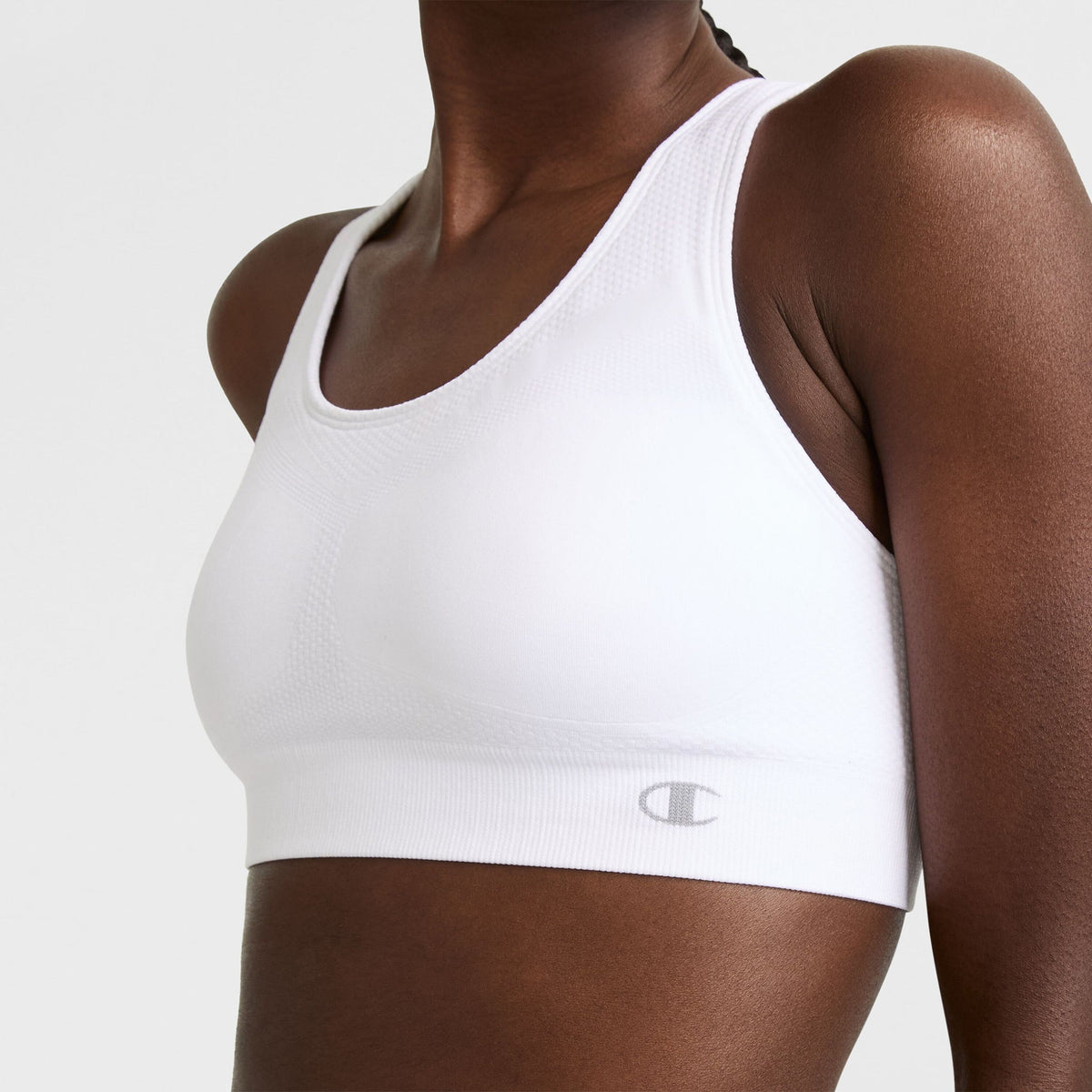 A person wears the Champion Seamless Racerback Sports Bra in white, featuring moderate support and a subtle logo on the band, shown from shoulders to waist against a plain background.