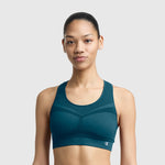 A woman models the Champion Seamless Racerback Sports Bra in teal, standing against a plain light gray background and looking at the camera with a neutral expression.