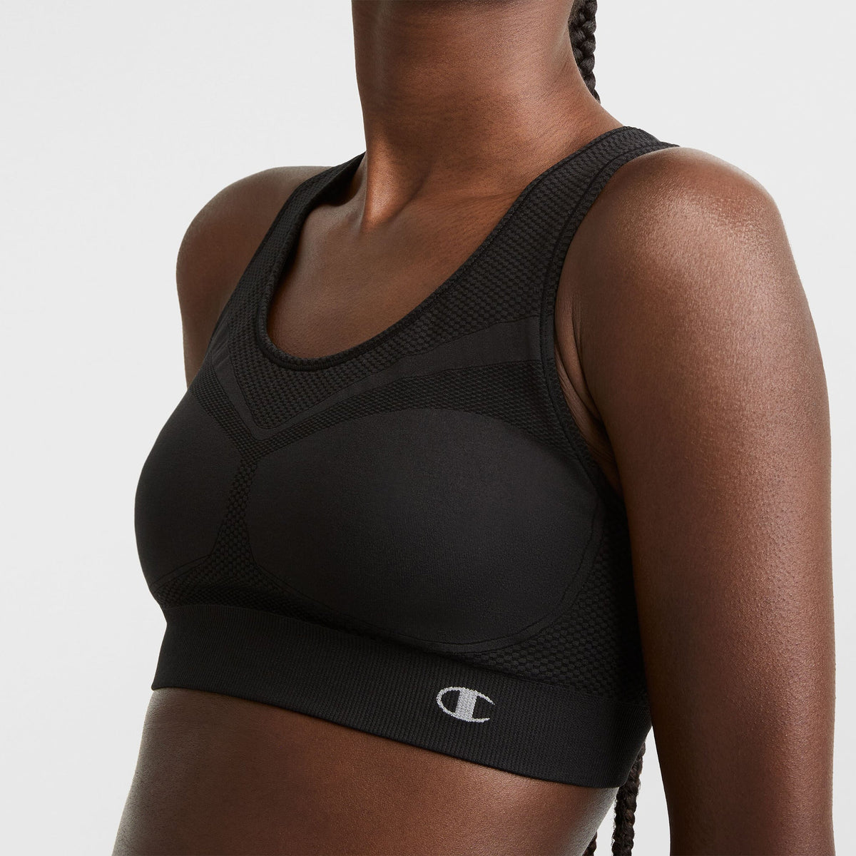 A person wearing a black sports bra with a mesh design and the Champion logo on the band, shown from the shoulders to the waist against a plain background.
