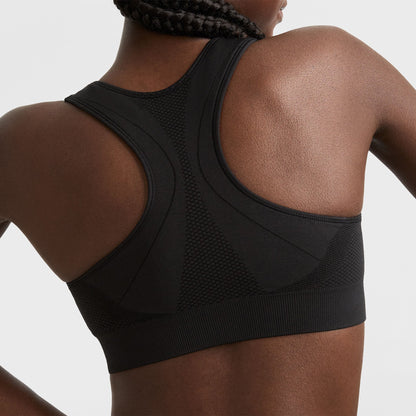 A woman with braided hair is shown from the back wearing a black racerback sports bra with textured panels and seamless detailing.