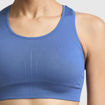 A person models the Champion Infinity Racerback Sports Bra in blue, seen from shoulders to just above the waist against a plain light background.