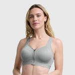 A woman with long blonde hair confidently models the Champion Motion Control Zip Sports Bra in light gray, standing against a plain background and looking at the camera.
