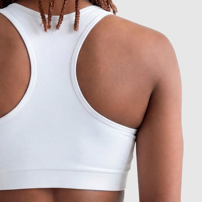 A person with medium brown skin and braided hair is shown from the back, wearing a white Champion Sports Bra, Script Logo, made of cotton-spandex jersey against a plain light gray background.