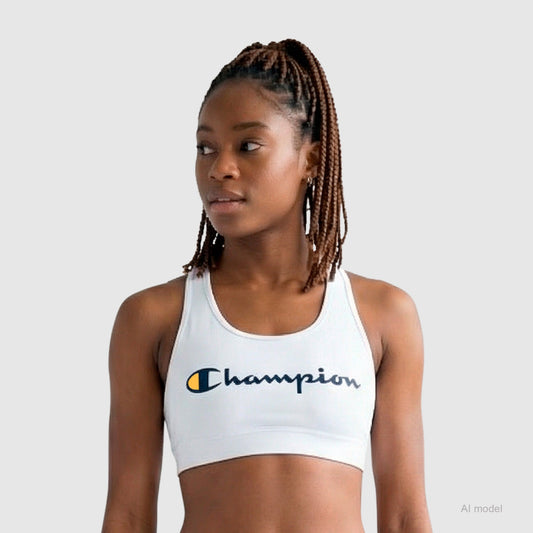 A woman with braided hair wears a white Champion Sports Bra, Script Logo, made from cotton-spandex jersey, standing against a plain light gray background and looking slightly to her left.