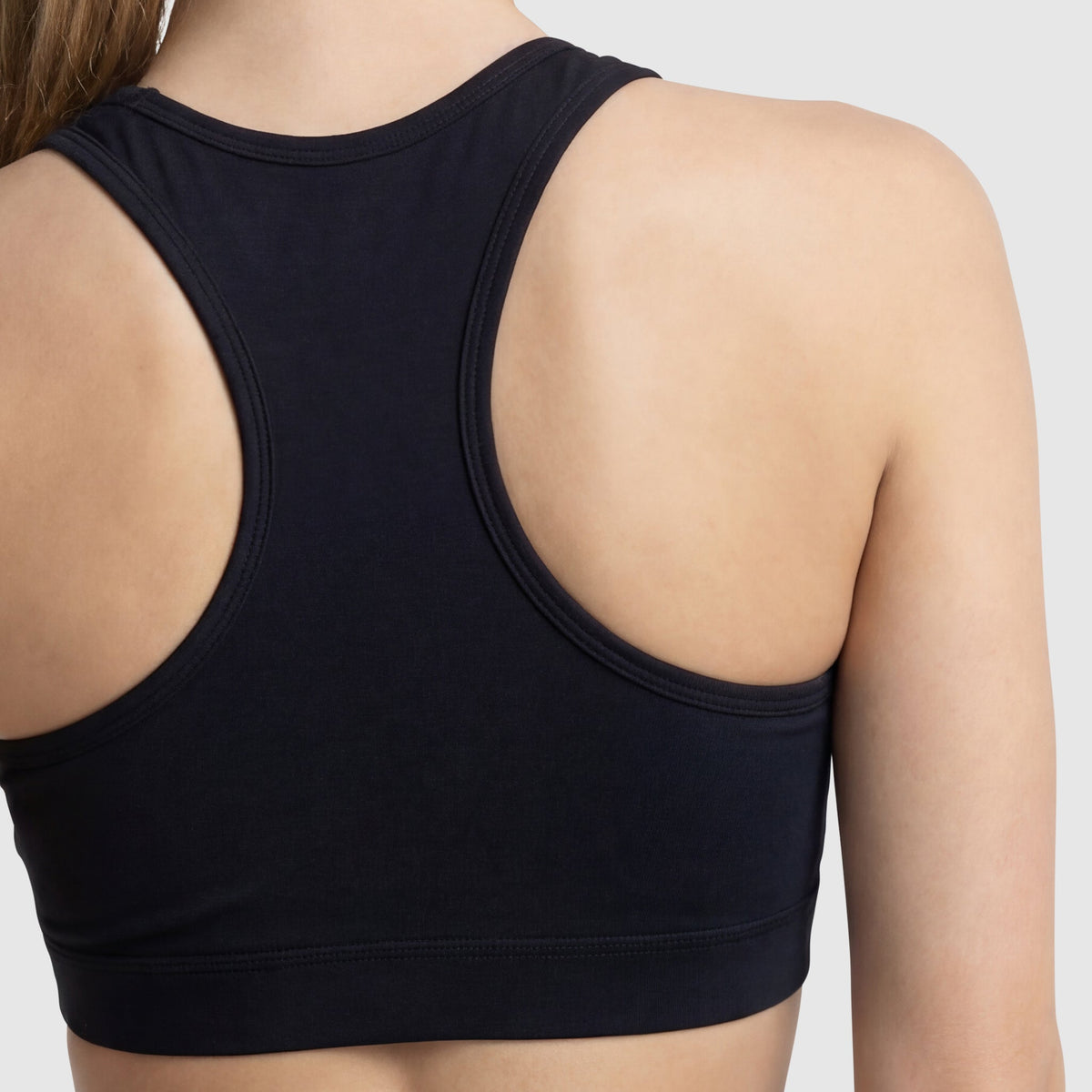 A close-up of a person’s upper back and shoulders wearing the Champion Sports Bra, Script Logo in black cotton-spandex jersey against a plain light background.