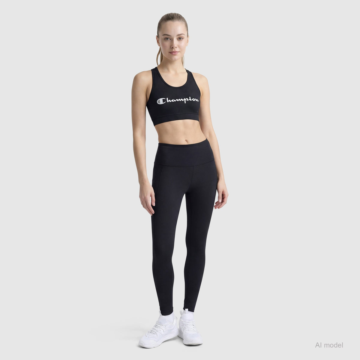 A woman faces forward against a plain light background wearing a black Champion Sports Bra, Script Logo, paired with black leggings and white sneakers.
