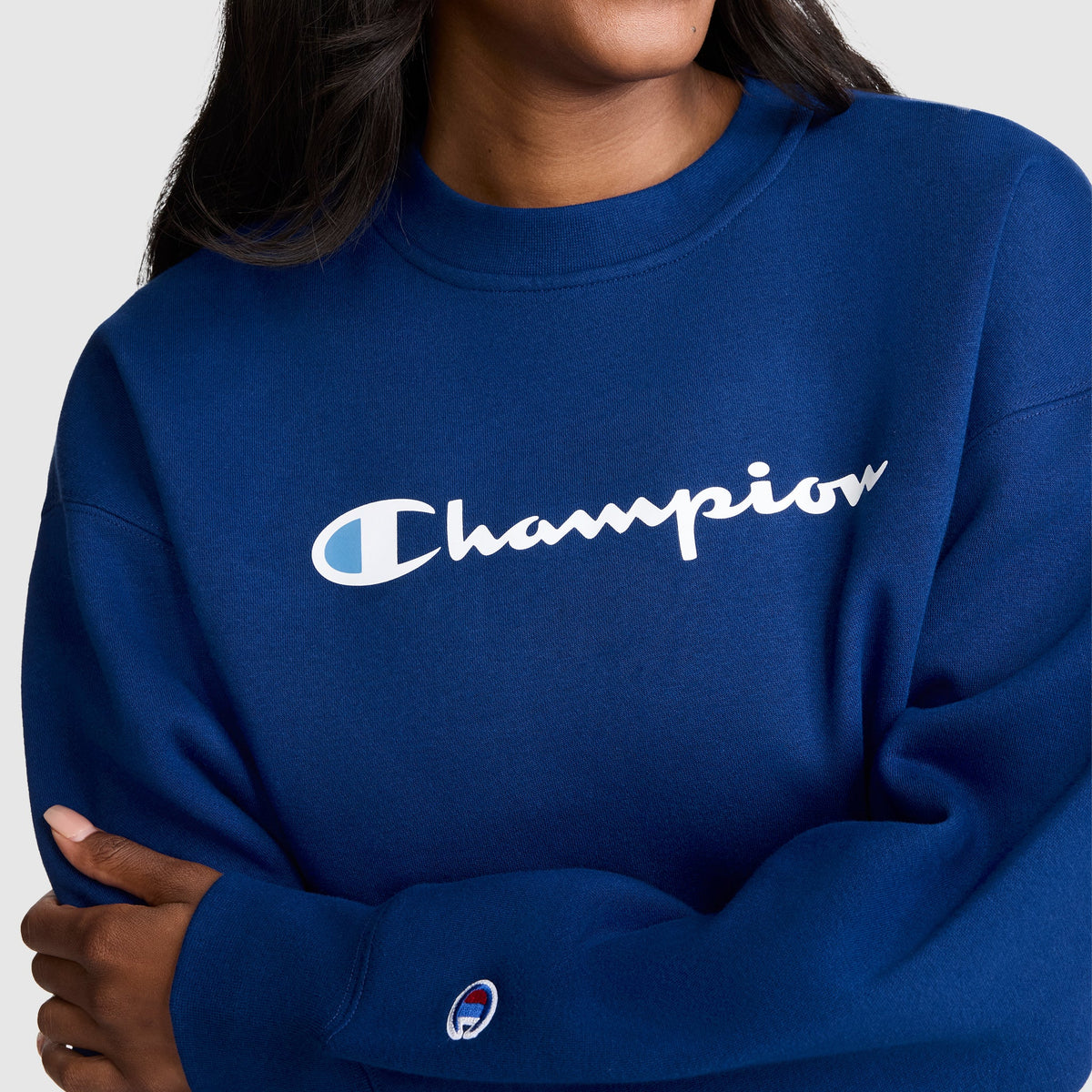 A person wearing the Champion Powerblend Crewneck Sweatshirt, Script Logo—a royal blue women’s crewneck featuring the signature white Champion script across the chest and a small logo patch on the sleeve. Made from cozy Powerblend fleece, this sweatshirt offers a blend of comfort and timeless style.