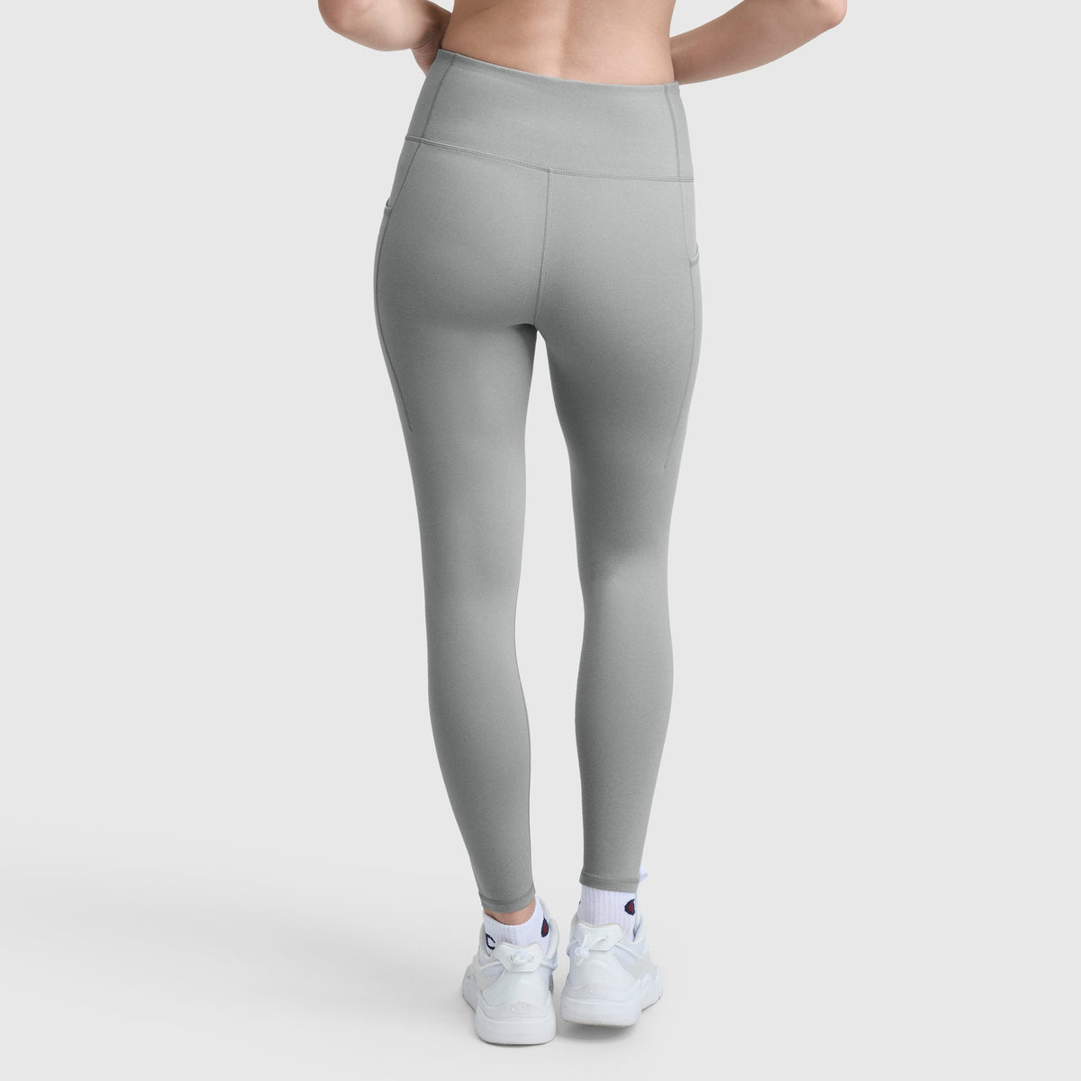 A person is shown from the back wearing Champion C Logo high-waisted, light gray stretch leggings with a wide waistband and white sneakers, standing against a plain white background. The leggings feature a smooth, fitted look.