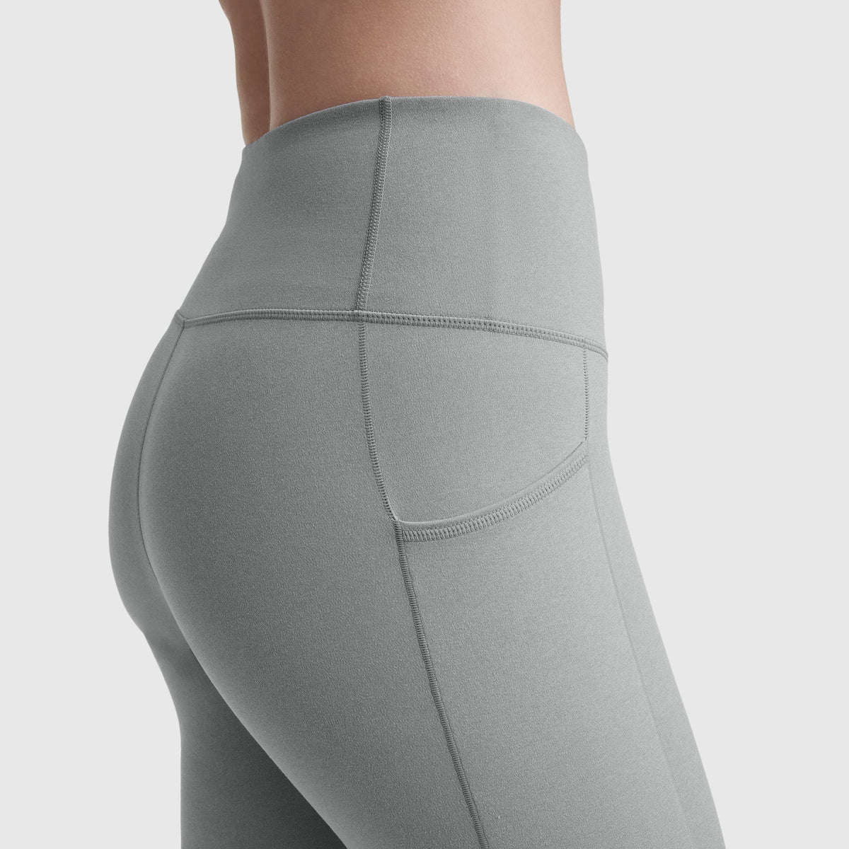 A close-up side view shows a person wearing Champion C Logo high-waisted light gray leggings with pockets and reinforced stitching, highlighting the silky soft comfort and practicality against a plain background.