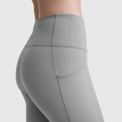 A close-up side view shows a person wearing Champion C Logo high-waisted light gray leggings with pockets and reinforced stitching, highlighting the silky soft comfort and practicality against a plain background.