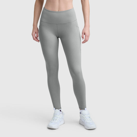 A person wears Champion C Logo light gray, high-waisted stretch leggings with pockets and white athletic shoes against a plain light background. The silky soft leggings have a smooth finish. The person's head is not visible.