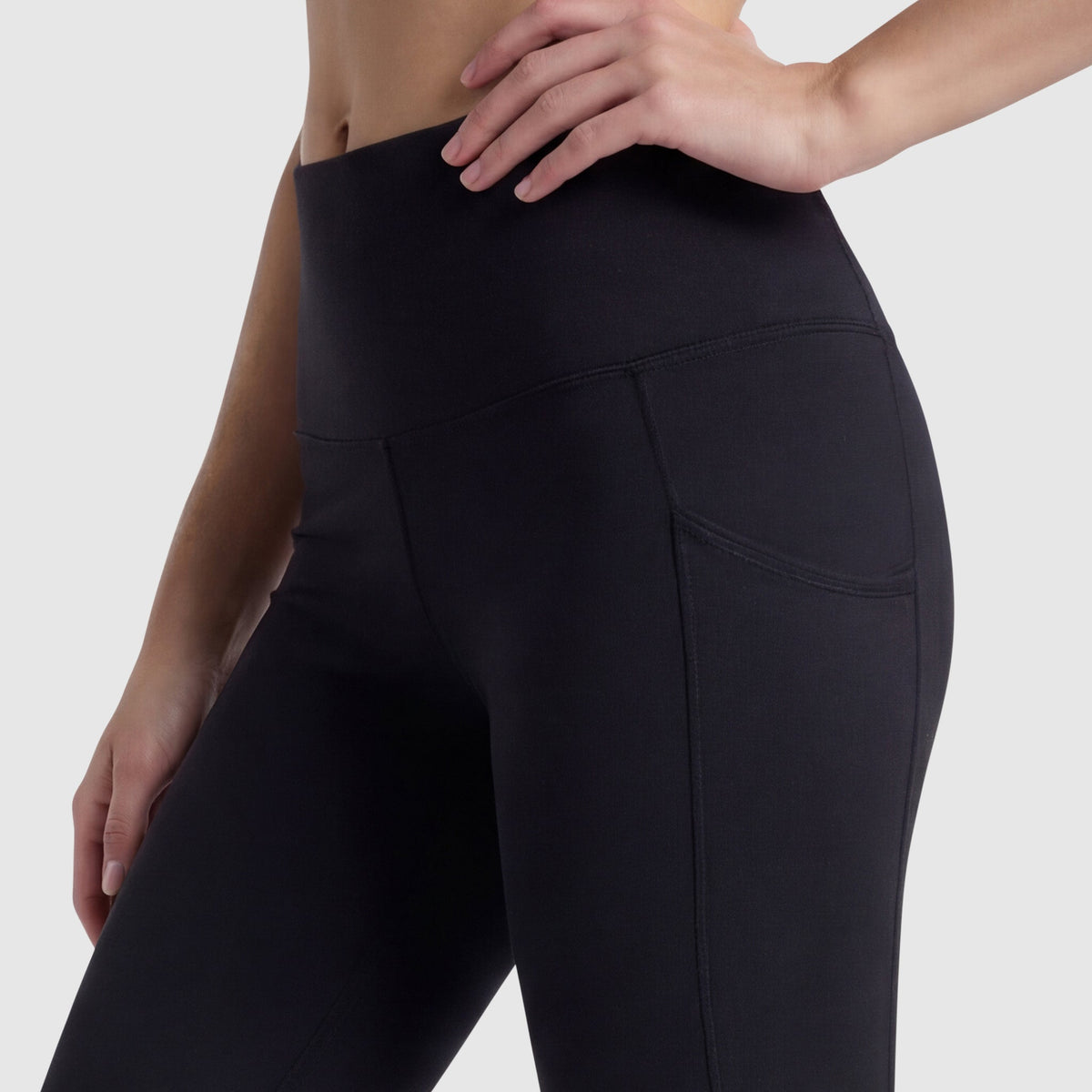 A person wears Champion C Logo high-waisted black leggings with side pockets, made from soft peached fabric, shown waist to mid-thigh against a plain light background, one hand resting on their hip.