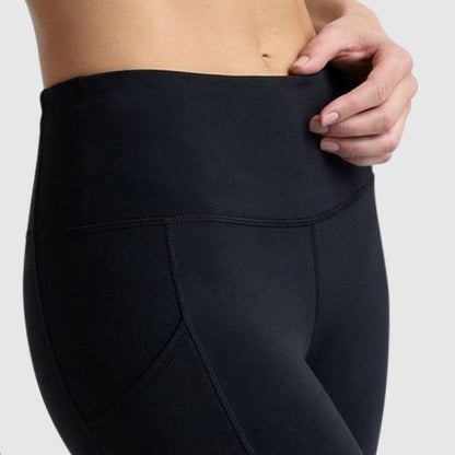 A close-up shows a person wearing Champion Leggings, C Logo in high-waisted black peached fabric, gently pulling at the waistband against a plain light background.