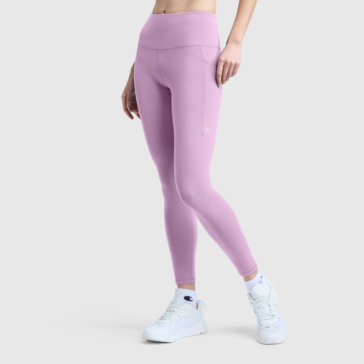 A person is shown from the waist down wearing Champion C Logo high-waisted, light purple silky soft leggings and white athletic shoes, standing against a plain light gray background.