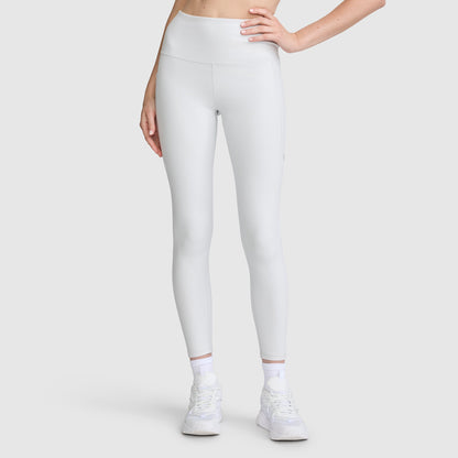 A person models the Champion C Logo Leggings, featuring a high-waisted white design with side pockets. Paired with white sneakers and socks, they stand against a plain light gray background, left hand resting on their hip and only the lower half of their body shown.